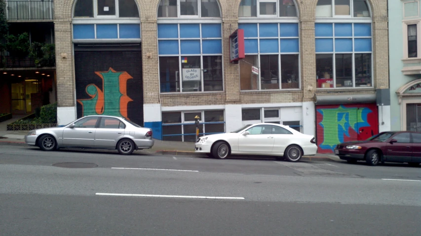 two white cars parked by the curb in front of a large building