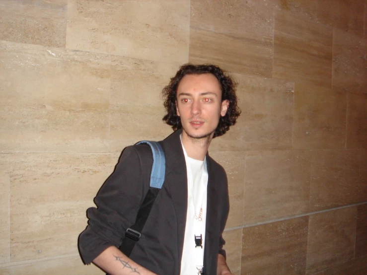 a man standing against a beige wall with a blue backpack