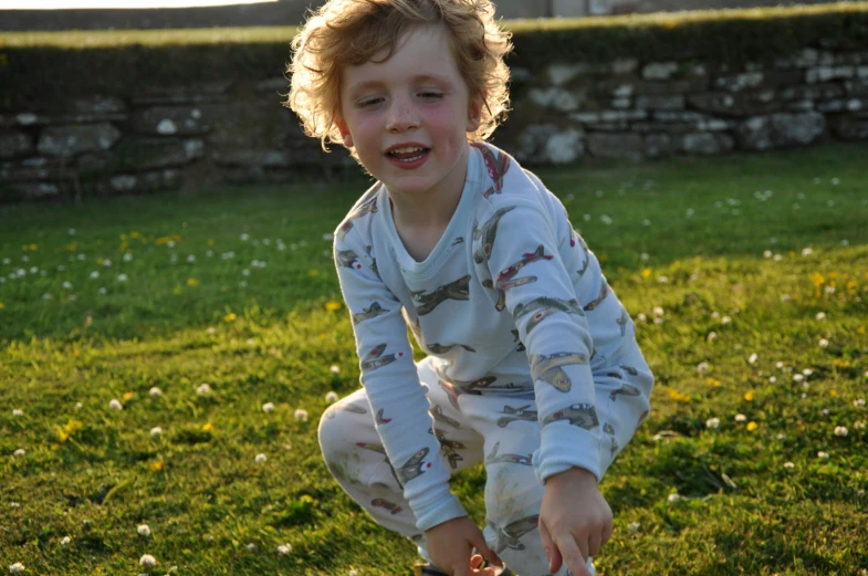 a little boy in his pajamas, picking soing up off the ground