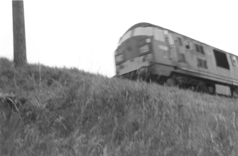 a black and white picture of a train moving down a grassy hill