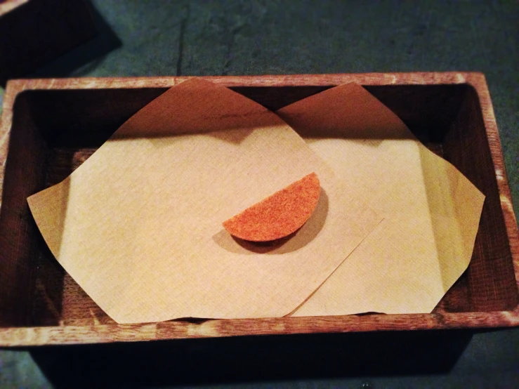 two paper napkins in a wood container, next to one slice of pizza