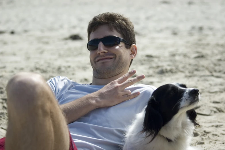 man sitting on the sand with a large white and black dog next to him