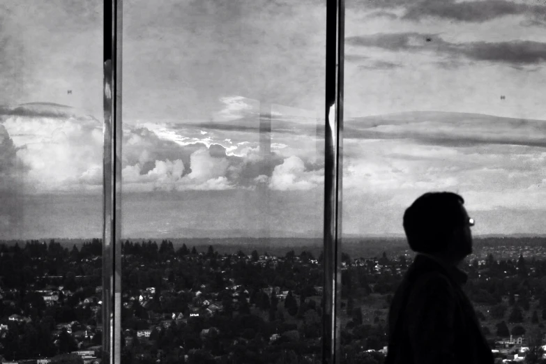 man looking out window overlooking city below