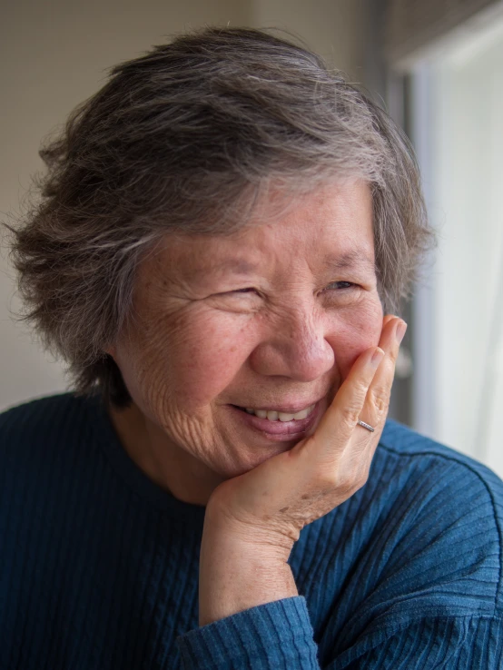 an older woman smiles in front of a window