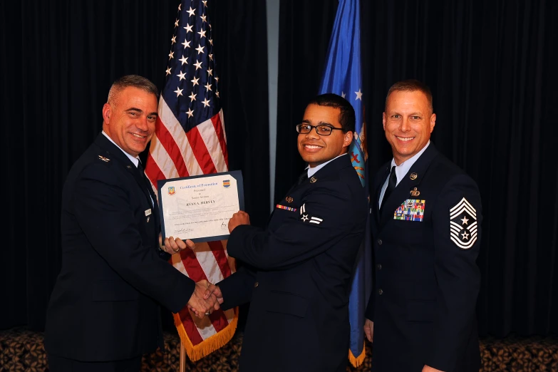 two men in service uniforms shaking hands with an american flag behind them