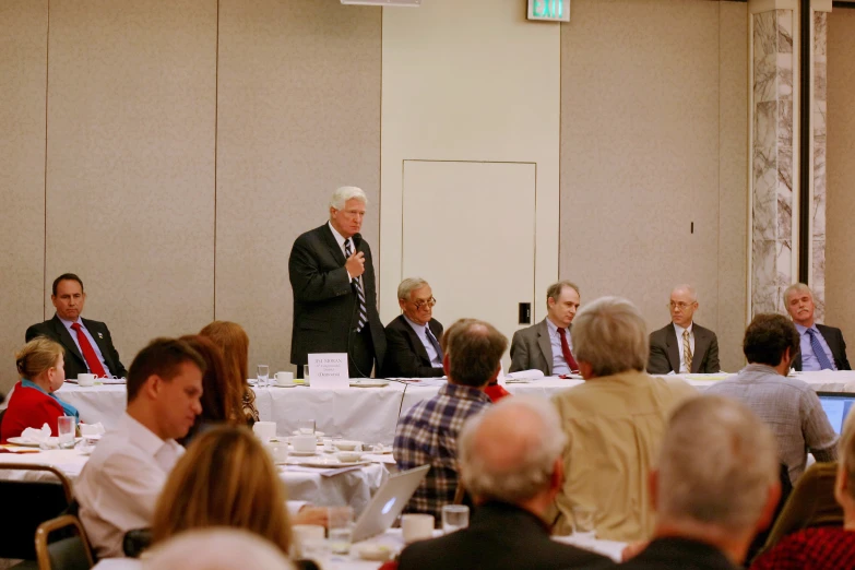 a group of people sitting at tables in front of a speaker