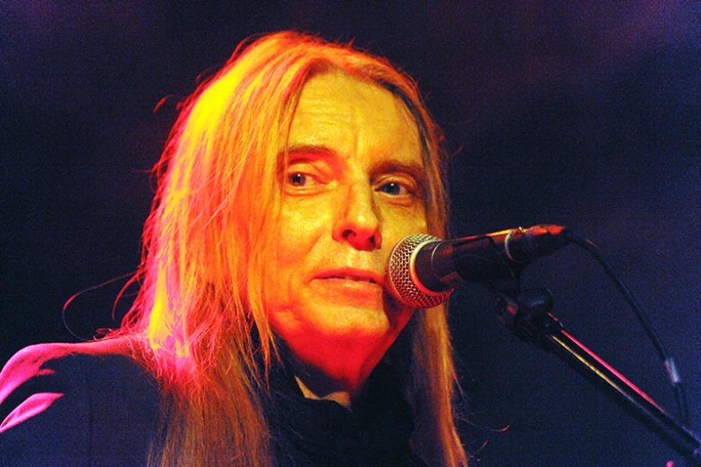 a man in black shirt standing at microphone with light shining on him