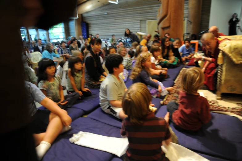 many children sit on small blue beds and watch others