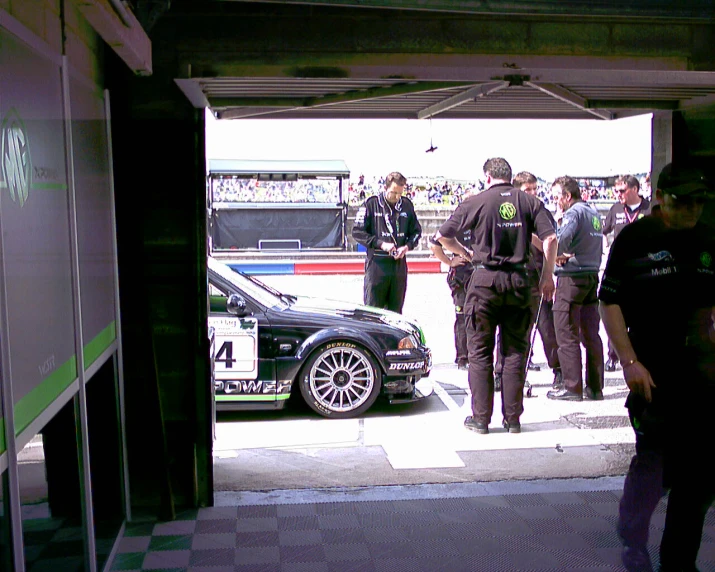 an auto racing car in the garage with several men and their cars