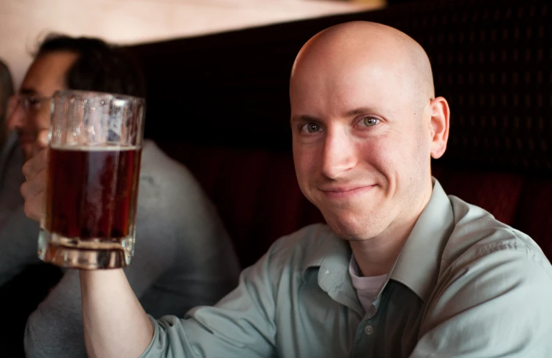 a bald man holding up a glass with liquid in it