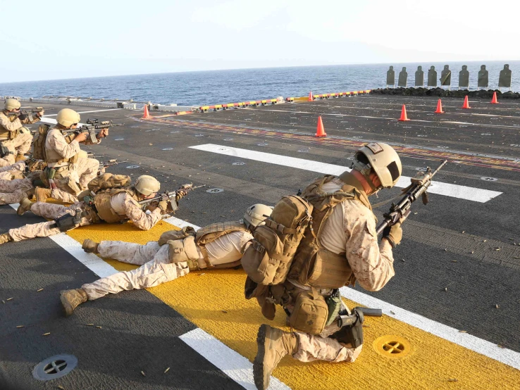 three soldiers sit and wait on a deck near a boat in the ocean