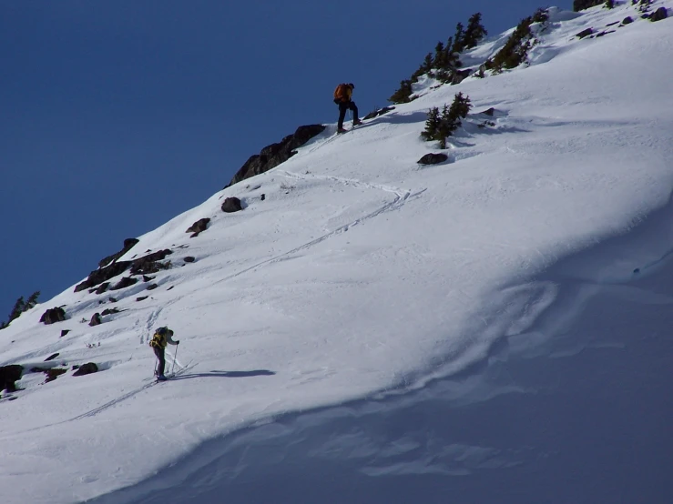two skiers heading down the steep side of a mountain