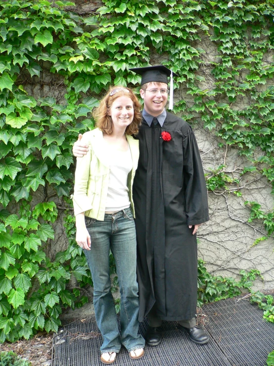 a woman poses with a male graduate in front of greenery