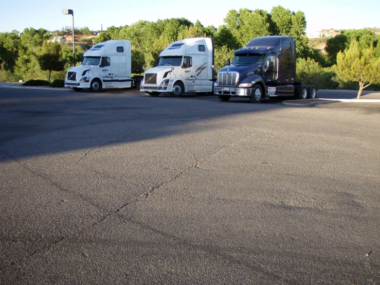 three semi trucks are parked in an empty lot