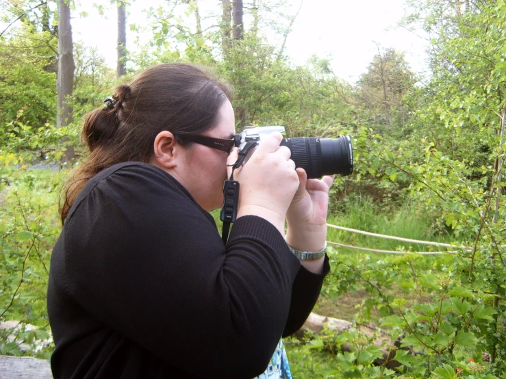 woman with large lens taking a po near bushes