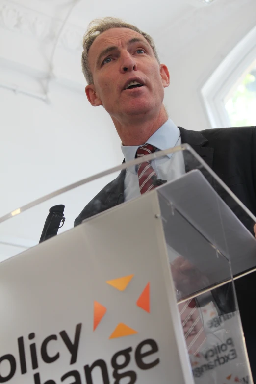 a man speaking at a political event and holding a piece of clear acrylic