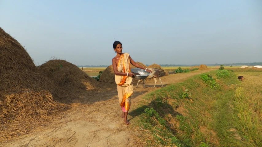 a woman walking down a dirt road next to hay