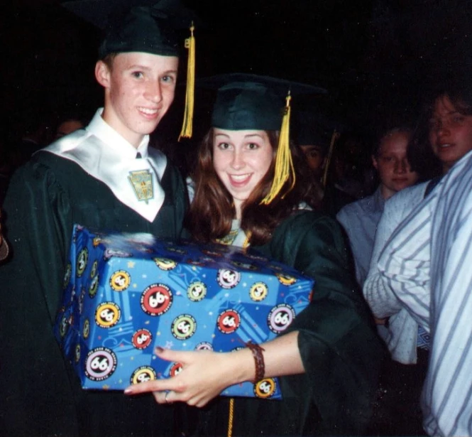 a boy and girl dressed in graduation clothes hold presents while standing beside each other