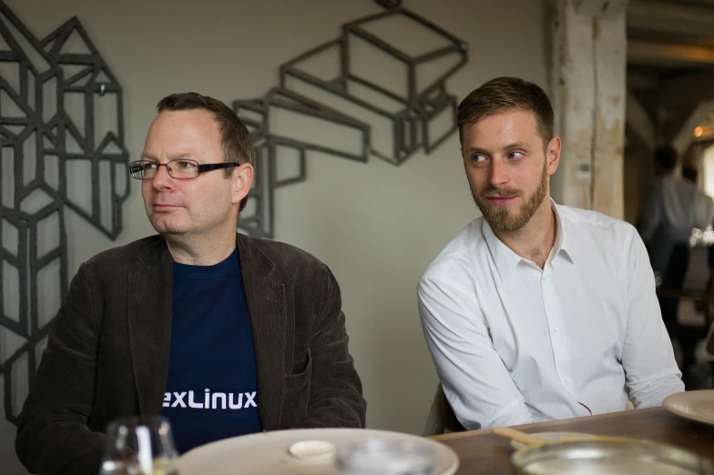 two men sitting down at a table in front of some plates and glasses