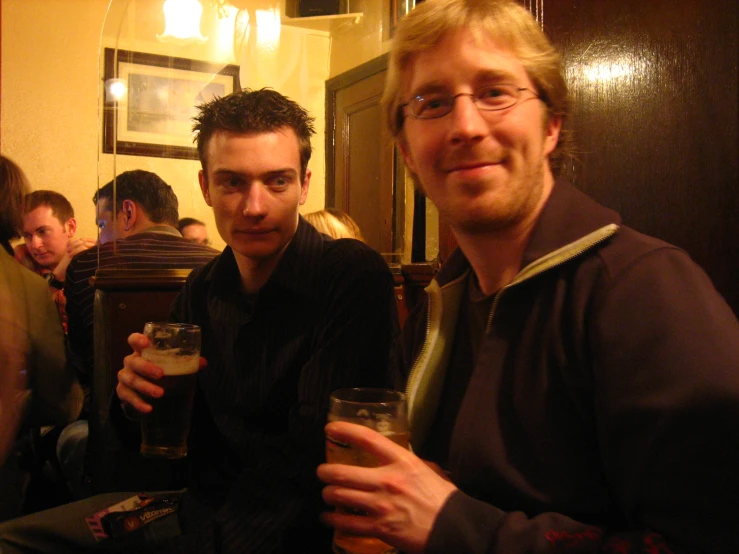 two men standing next to each other holding beverages