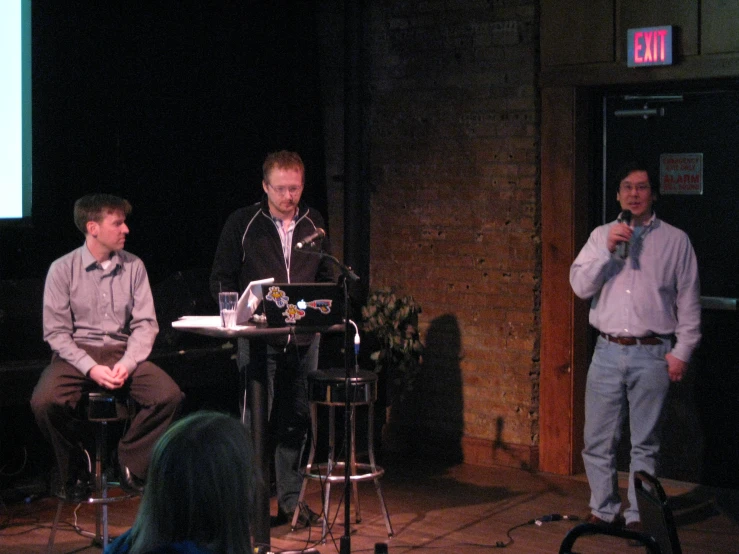 three men sitting at chairs speaking into microphones