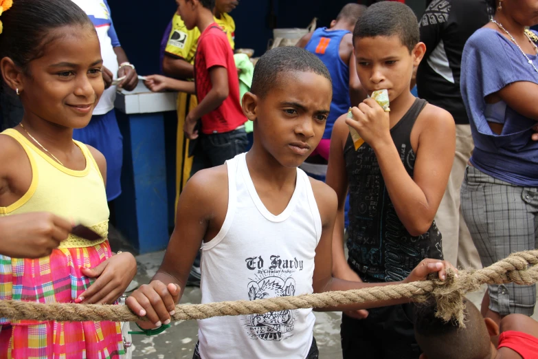 three children stand next to each other, and one boy holds a rope