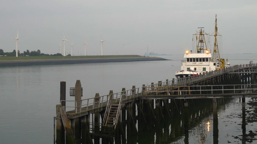 boat on calm water sitting at pier by wind mills