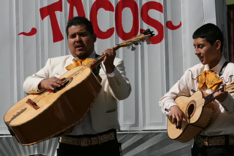 two men are playing ukulele in front of a sign