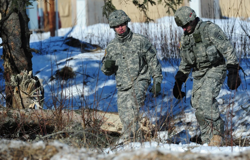 two military men in camouflage walk through the snow