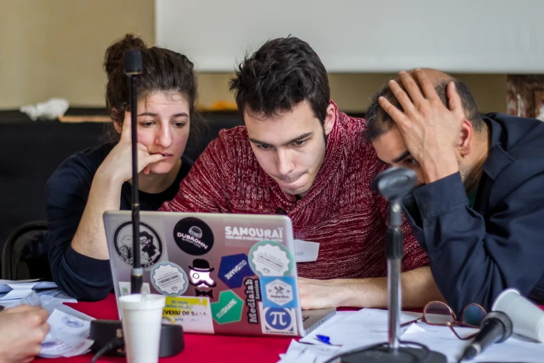 a group of young men and women sitting at a table looking at a laptop screen