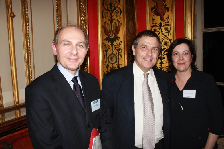 three people wearing formal wear and standing in front of wall with gold panels