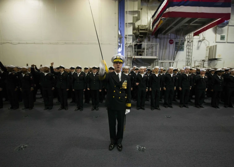 navy captain standing in front of his group and a flag