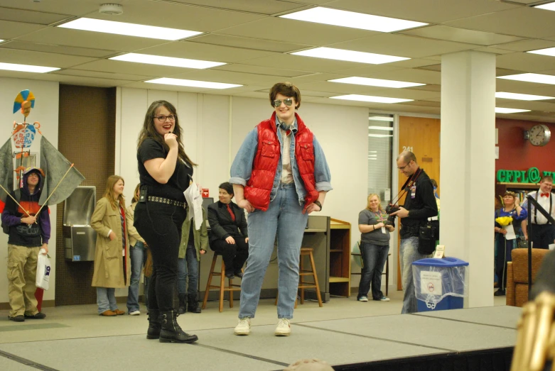 two people are on a stage as one of them is holding a microphone and two others watch