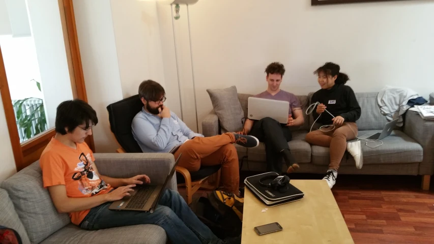 four young men sitting on couches in an apartment with laptop computers