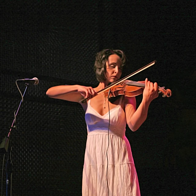 a woman holding a violin while standing next to a microphone