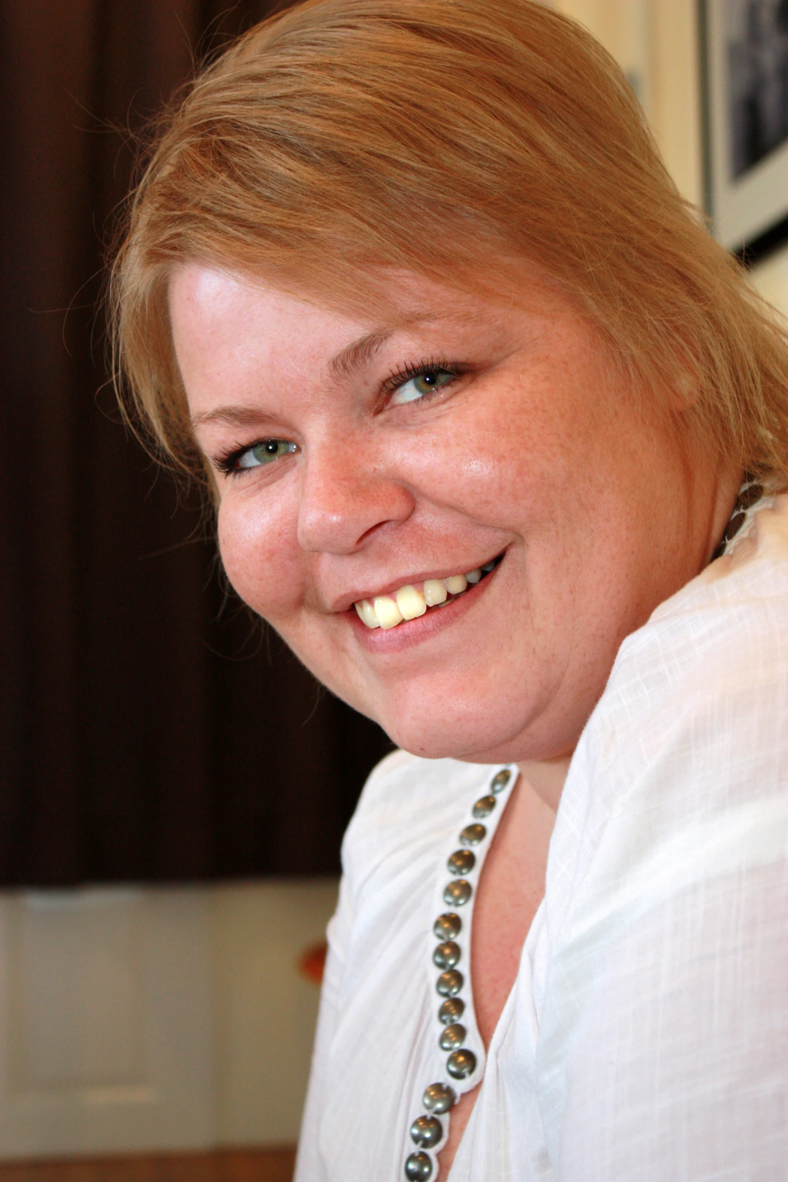 an attractive woman in a white top and necklace smiles