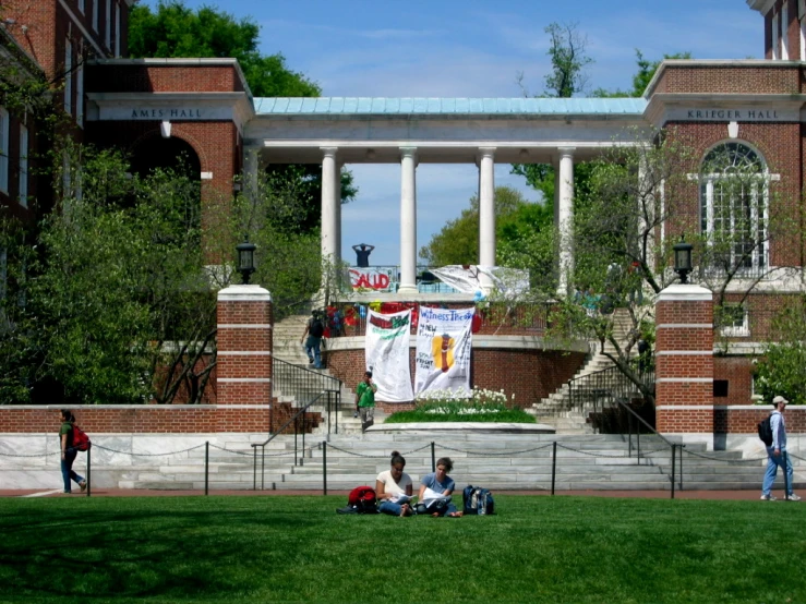 some students sitting in the grass with a building and flags behind them