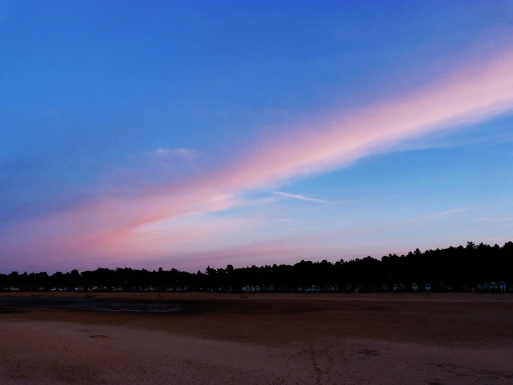 a beach at dusk with a plane flying in the sky