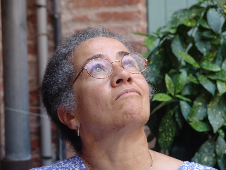 a woman with glasses looks up with a plant in the background