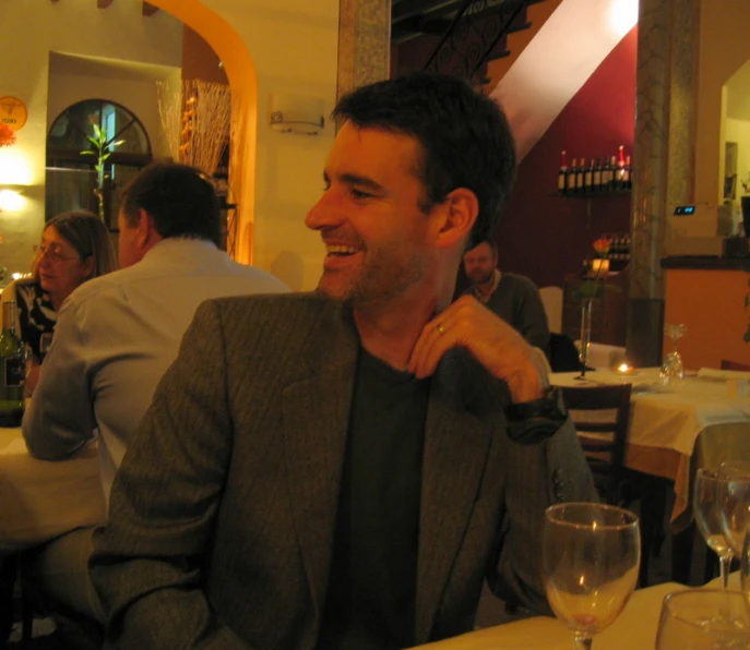 man in a business jacket sitting at a table smiling