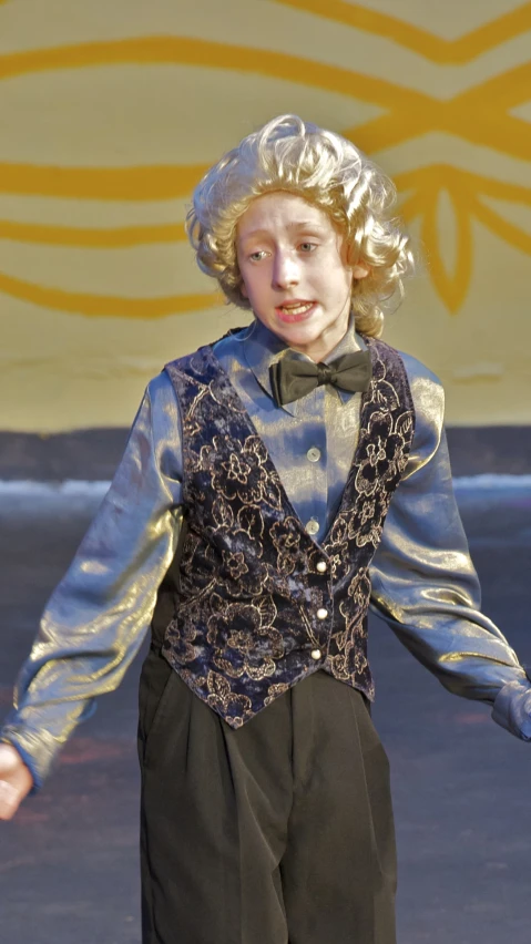 a boy in a vest and bow tie walking on a stage