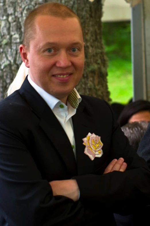 the man is dressed in a suit and posing with his arms crossed