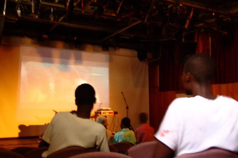 two men at the front of a room watching a screen