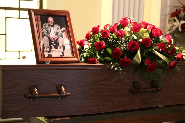 a casket with flowers on it and a framed po