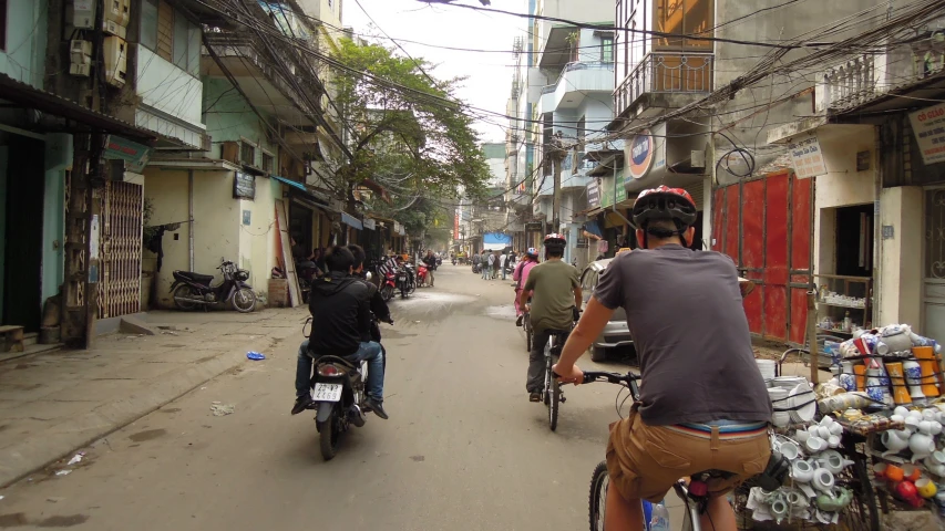 some people riding bikes down the street by some buildings