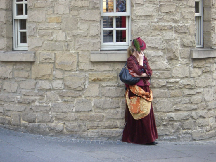 a woman is standing by a brick building and talking on her phone