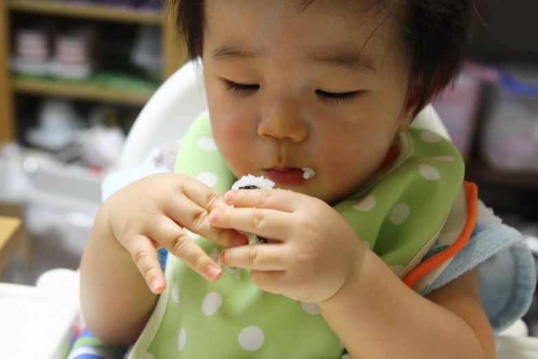 a small child sitting in a high chair eating soing white