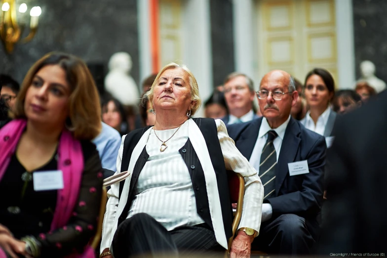 several people in suits sitting down and one of them is wearing a striped shirt