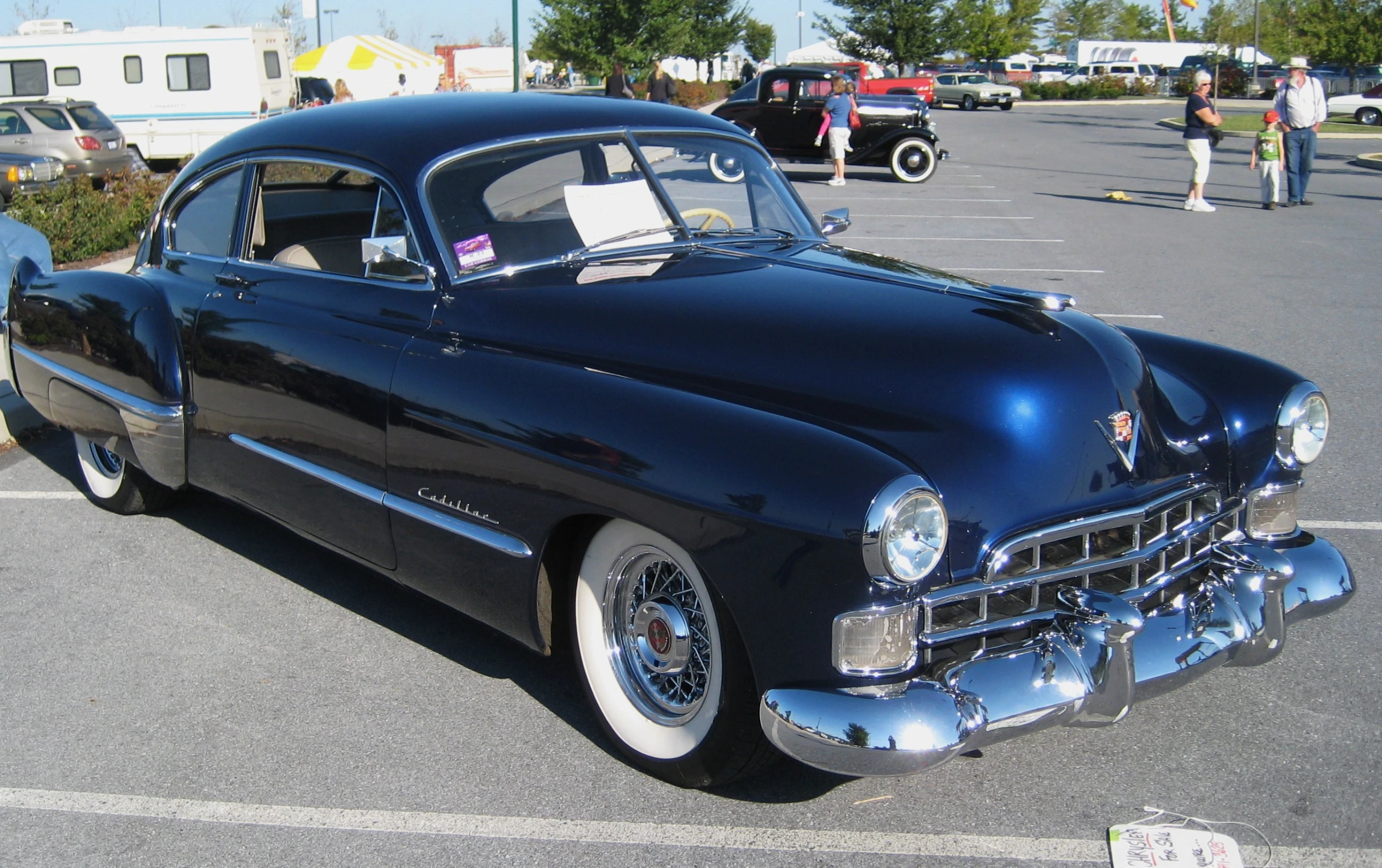 a black classic car in parking lot at an outdoor event