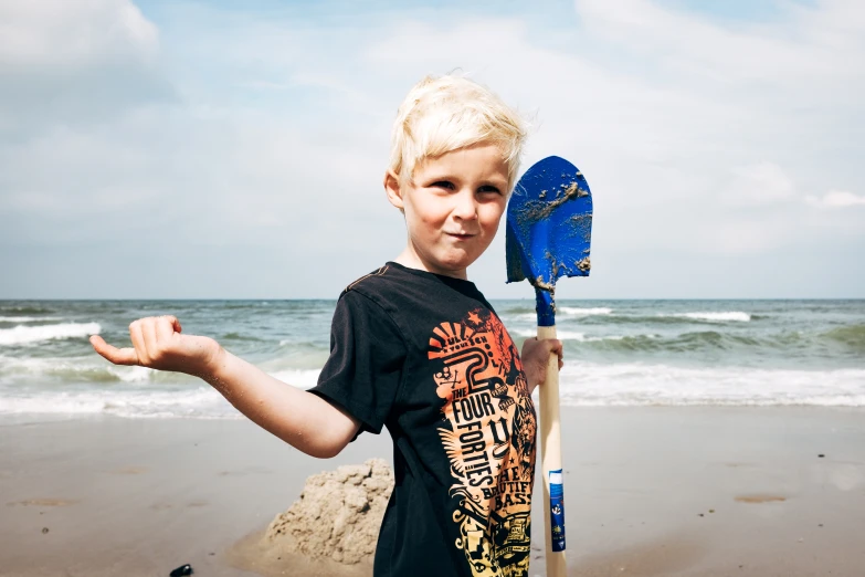 the boy holds his surfboard and stands on the beach